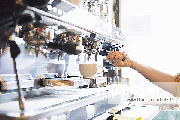 Hand einer weiblichen Barista  die eine Espressomaschine in einem Kaffeegeschäft bedient