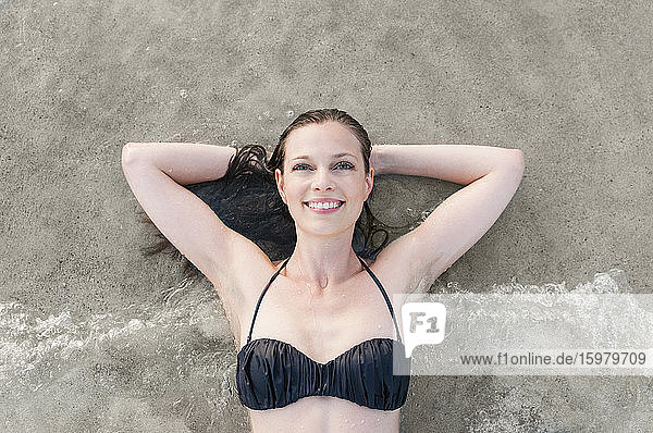 Portrait of happy woman in bikini lying at seashore  Sardinia  Italy