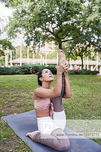 Mittlere erwachsene Frau übt Yoga auf einer Matte im Park