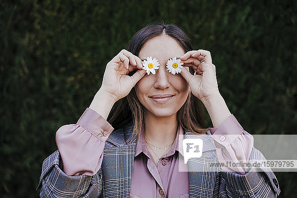 Portrait of smiling woman covering her eyes with marguerites