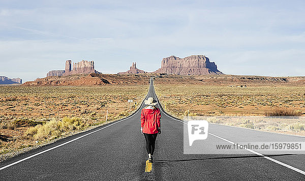 Rückansicht in voller Länge einer weiblichen Touristin  die auf einer Wüstenstraße läuft  Monument Valley Tribal Park  Utah  USA