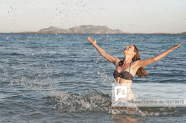 Happy woman in bikini standing in the sea splashing with water  Sardinia  Italy