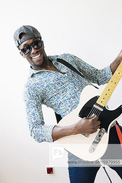 Porträt eines glücklichen jungen Popmusikers  der Gitarre vor weißem Hintergrund spielt