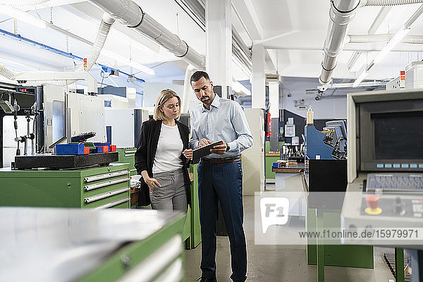 Businessman and woman using tablet in factory hall