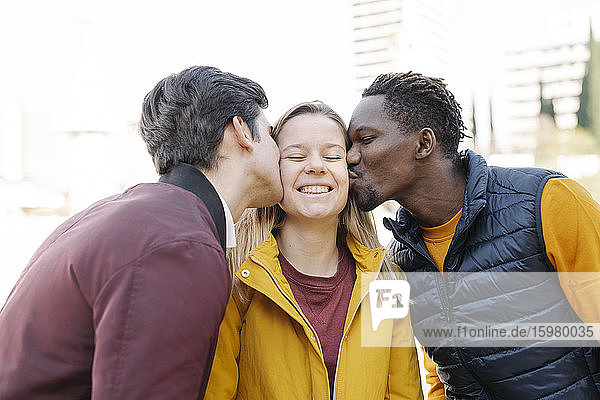 Two young men kissing smiling young woman outdoors