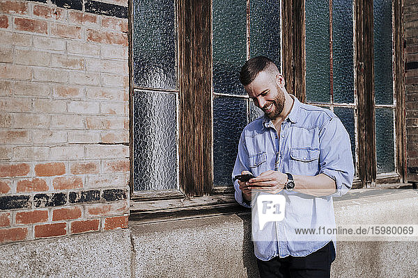 Lächelnder junger Mann schaut im Freien auf sein Handy