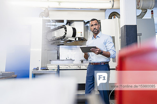 Businessman holding tablet at a machine in factory hall