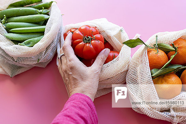 Hand of woman picking up fresh tomato from eco-friendly reusable mesh bag