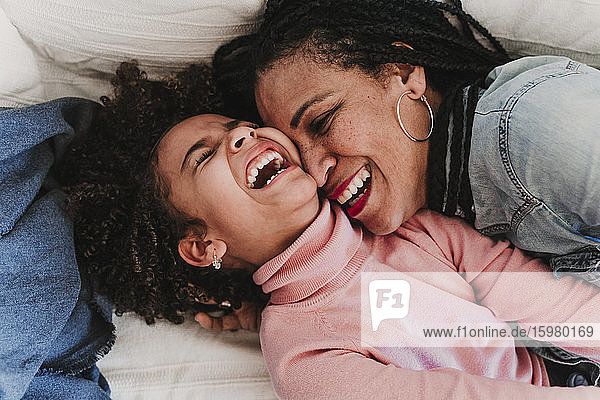 Porträt eines lachenden kleinen Mädchens und ihrer Mutter  die sich gemeinsam zu Hause amüsieren