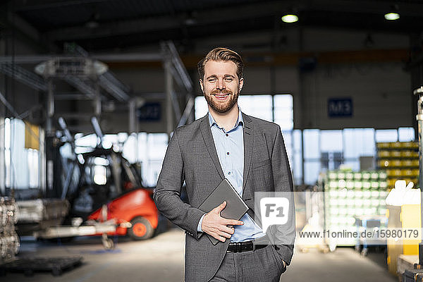 Portrait of a smiling young businessman with tablet in a factory