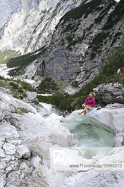 Reife Frau genießt beim Spritzen von Wasser mit dem Bein im Bach gegen den Berg