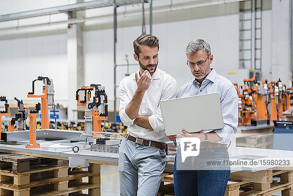 Two men using laptop on factory shop floor