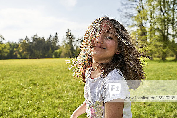 Playful girl with tousled hair standing on grass during sunny day