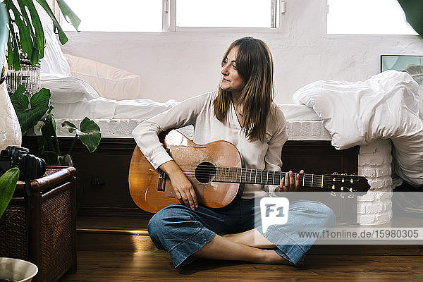 Frau sitzt auf dem Boden vor dem Bett mit Gitarre