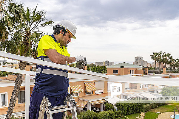 Älterer männlicher Techniker  der ein Solarpanel auf dem Dach installiert  während er gegen den Himmel steht