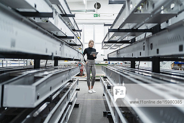 Frau mit Tablette an Metallstäben in Fabrikhalle