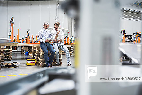 Two men sharing tablet on factory shop floor