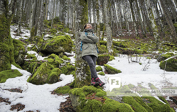 Frau lehnt an einer Buche im Nordschwarzwald mit Schneeresten im Frühling