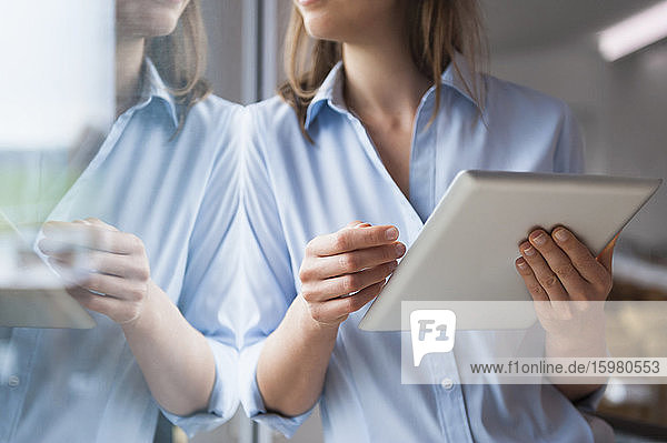 Mittlere erwachsene Frau  die ein digitales Tablet benutzt  während sie zu Hause am Fenster steht