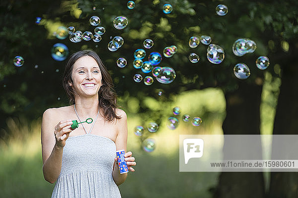 Glückliche junge Frau genießt beim Betrachten von Seifenblasen im Park