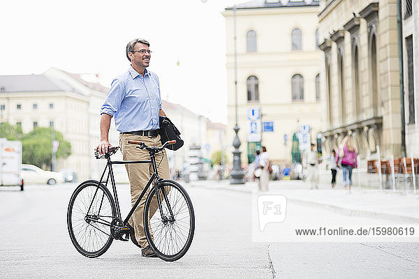 Smiling businessman looking away while walking with bicycle on road in city