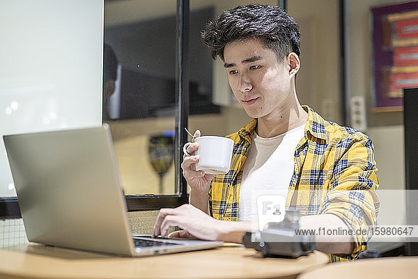Porträt eines jungen Touristen mit einer Tasse Kaffee in einer Herberge und einem Laptop