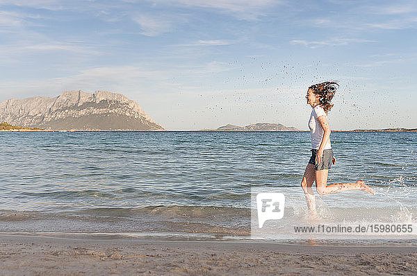 Glückliche Frau  die am Meer läuft und mit Wasser spritzt  Sardinien  Italien