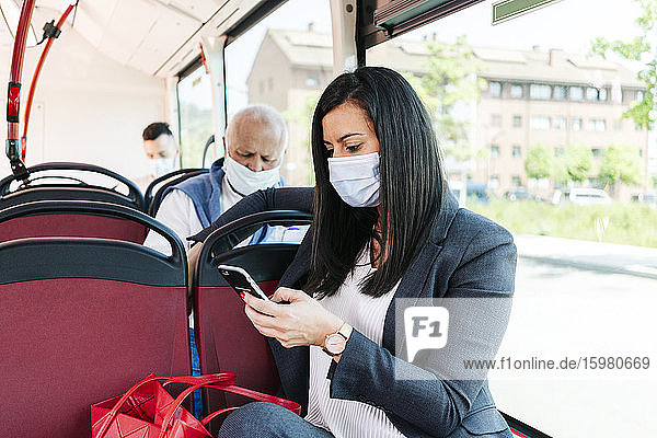 Geschäftsfrau mit Schutzmaske in einem öffentlichen Bus  die auf ihr Handy schaut  Spanien