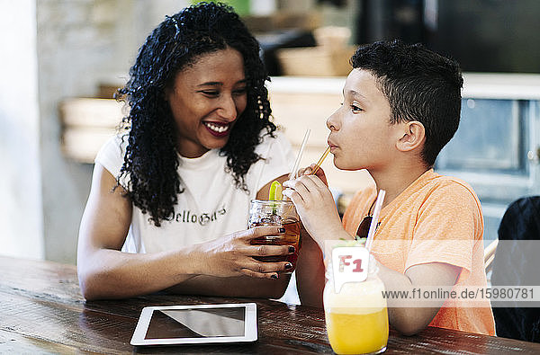 Lächelnde Frau  die ihr Getränk mit ihrem Sohn im Restaurant teilt