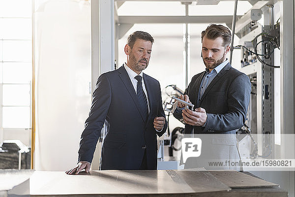 Two businessmen having a meeting in a factory examining workpiece