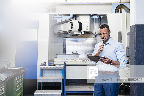 Geschäftsmann mit Tablet an einer Maschine in einer Fabrikhalle