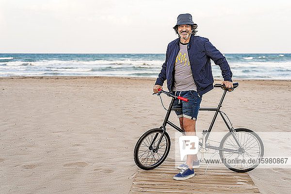 Mature man with bicycle  standing on the beach  smiling