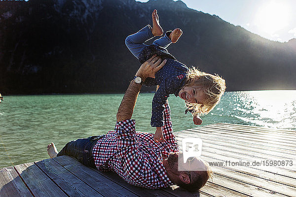 Vater hält seine glückliche Tochter im Arm  während er auf der Uferpromenade am Achensee liegt  Bundesland Tirol  Österreich