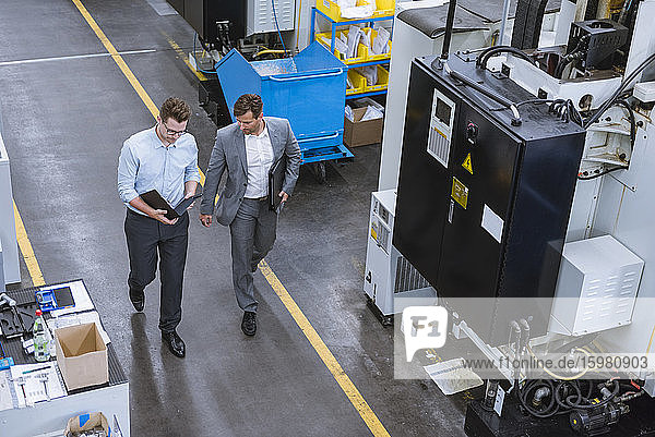 Two businessmen with clipboard walking and talking in factory