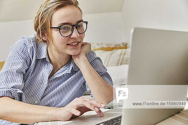 Porträt einer lächelnden jungen Frau  die zu Hause einen Laptop benutzt