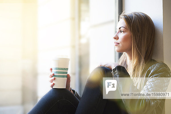 Frau schaut durch das Fenster und hält einen Einweg-Kaffeebecher in einem Café