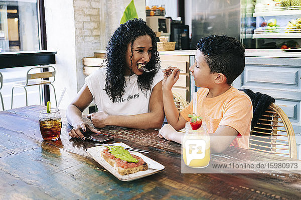 Junge füttert glückliche Mutter mit Gabel  während er im Restaurant sitzt