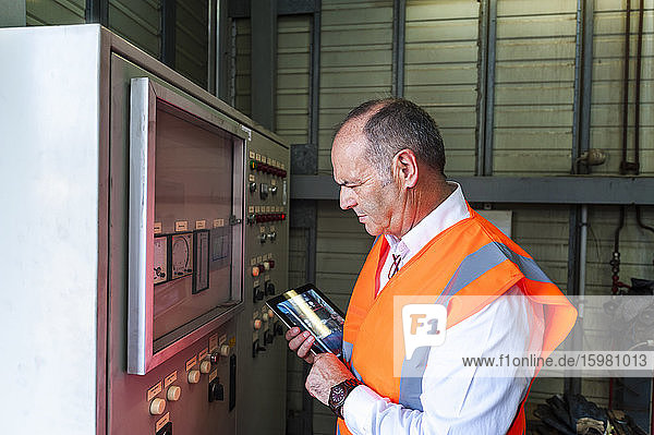 Senior man with tablet wearing safety vest examining a machine