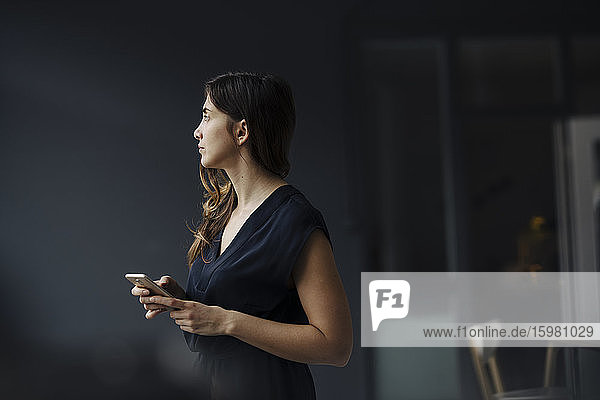 Nachdenkliche junge Geschäftsfrau mit Smartphone in einem Loft