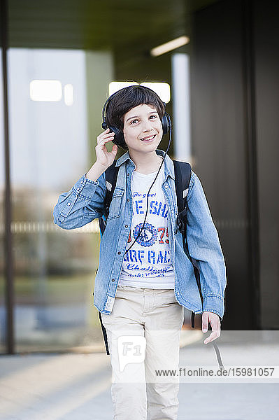 Glücklicher Junge  der beim Gehen auf der Straße über Kopfhörer Musik hört