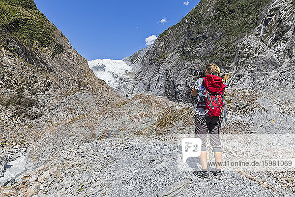Neuseeland  Westland District  Franz Josef  Weibliche Rucksacktouristin beim Fotografieren im Franz Josef Gletscher