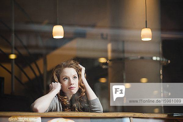 Nachdenkliche Frau  die sich auf einen Tisch stützt  gesehen durch das Fenster eines Cafés