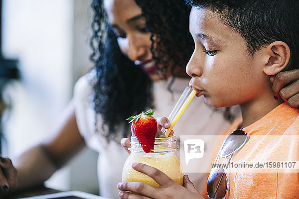 Nahaufnahme eines Jungen  der einen Smoothie aus einem Strohhalm trinkt  während er neben seiner Mutter im Restaurant sitzt