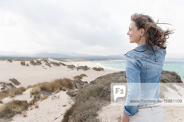 Happy woman with blowing hair standing in the dunes enjoying view  Sardinia  Italy