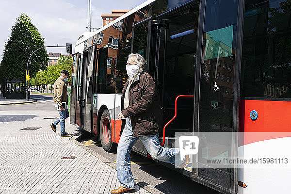 Älterer Mann mit Schutzmaske beim Aussteigen aus einem öffentlichen Bus  Spanien