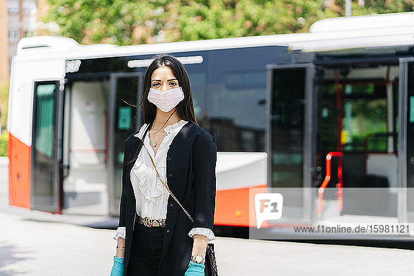 Porträt einer jungen Frau mit Schutzmaske und Handschuhen  die an einer Bushaltestelle wartet  Spanien