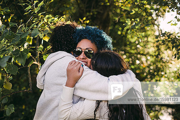 Liebevolle Kinder umarmen Mutter mit blauem Haar vor Bäumen im Park