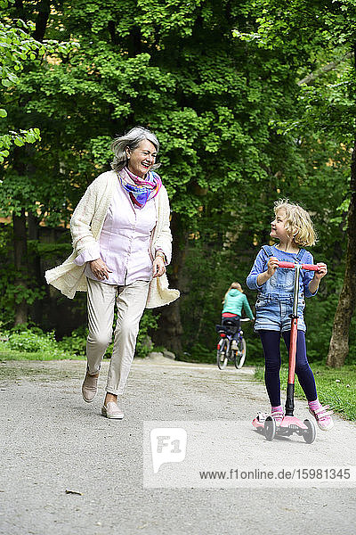 Active senior woman running while granddaughter riding push scooter in park