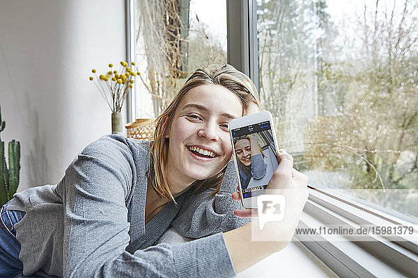 Porträt einer glücklichen jungen Frau  die ein Selfie auf dem Display eines Smartphones macht