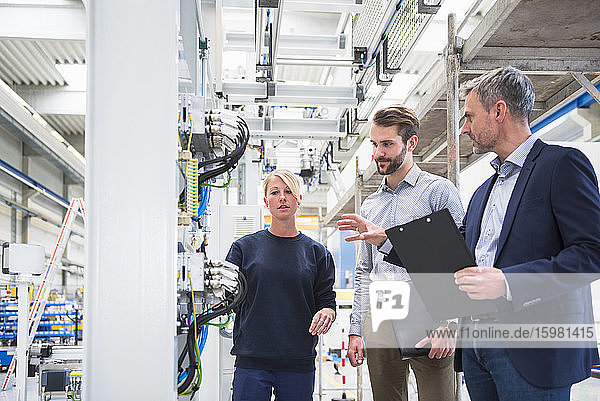 Two men and a woman talking in a factory
